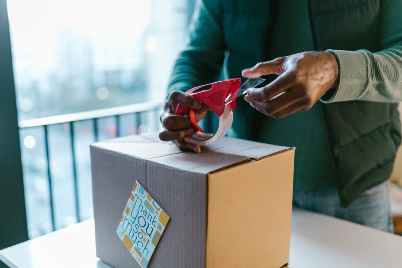 Close-up of man sealing a cardboard box with a tape dispenser indoors.